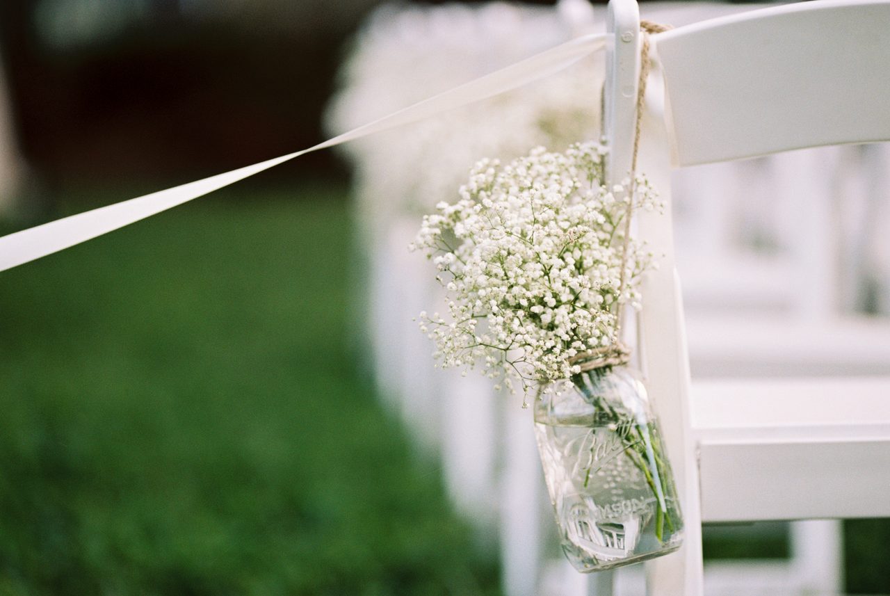 Mason jar with baby's breath hanging from a white chair in a garden aisle